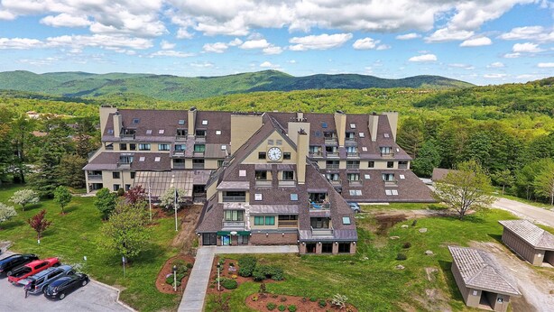 A multi-story hotel with a central clock tower, surrounded by lush greenery and mountains in the background. - Mountain Green Resort by Killington VR - 2 Bedrooms (Killington)