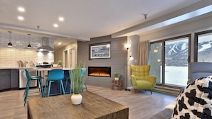 A modern living room with a fireplace, a dining area, and a kitchen. - Mountain Green Resort by Killington VR - 2 Bedrooms (Killington)