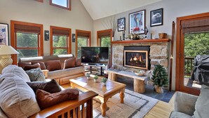 A spacious living room with a fireplace, large windows, and a television. - Cortina Mountain Chalet - Outdoor Hot Tub - Close To Pico And Killington Mountains 3 Bedroom Home (Rutland)