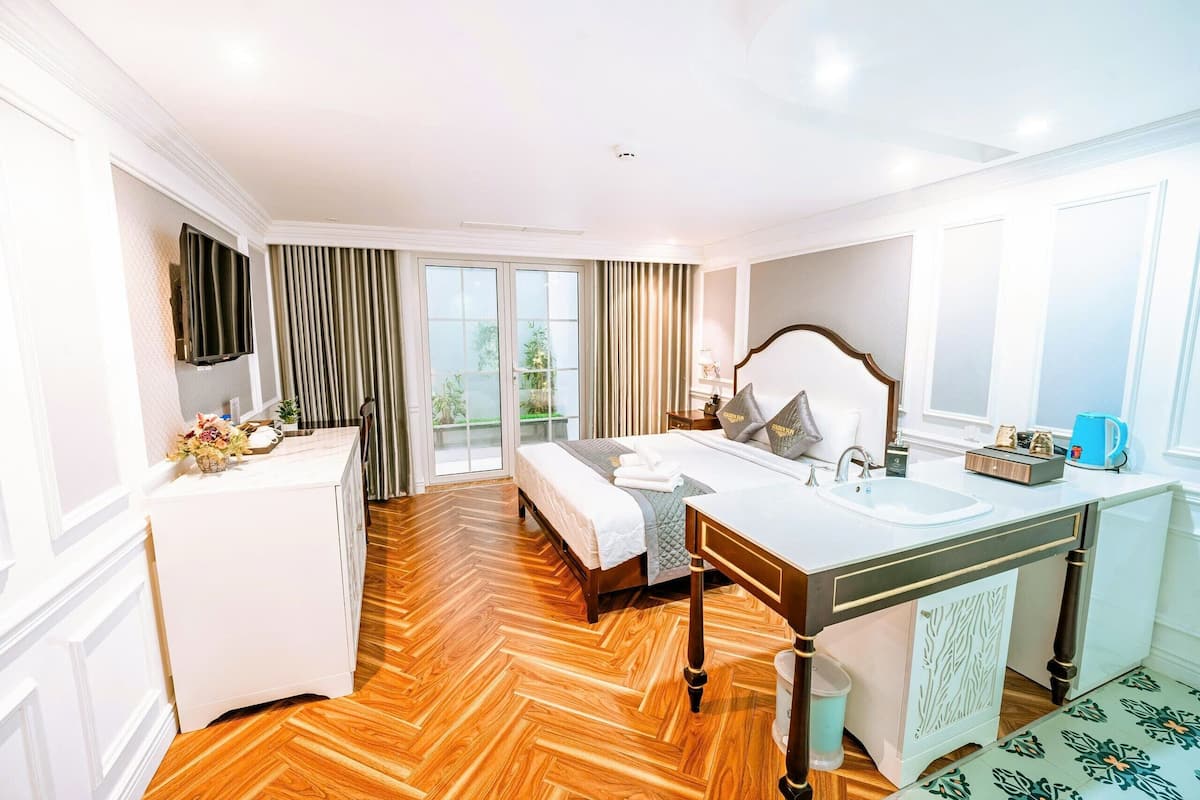 A hotel room with a bed, a double sink, a mirror, a television, and a window with curtains.