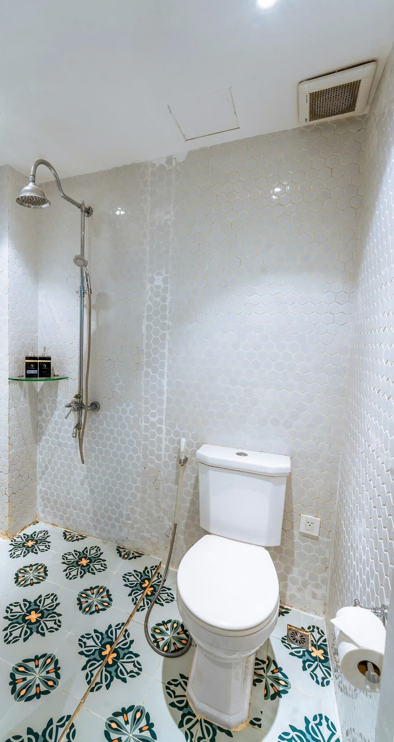 Une salle de bain avec des toilettes, une douche et un mur orné d’un motif hexagonal.