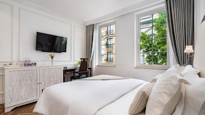 Ein Hotelzimmer mit einem großen Bett, einem an der Wand befestigten Fernseher, einem Schreibtisch mit Stuhl und einem Fenster mit Vorhängen.