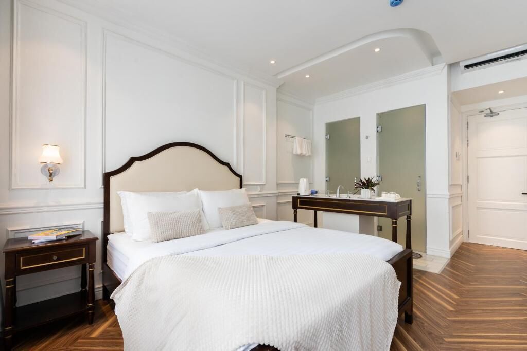 A hotel room with a large bed, a bedside table, a nightstand, a mirror, and a door leading to another room.