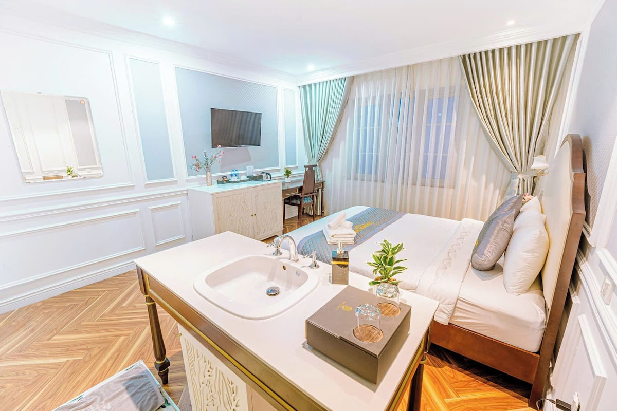 A hotel room with a bed, a desk with a sink, a television, and a window with curtains.