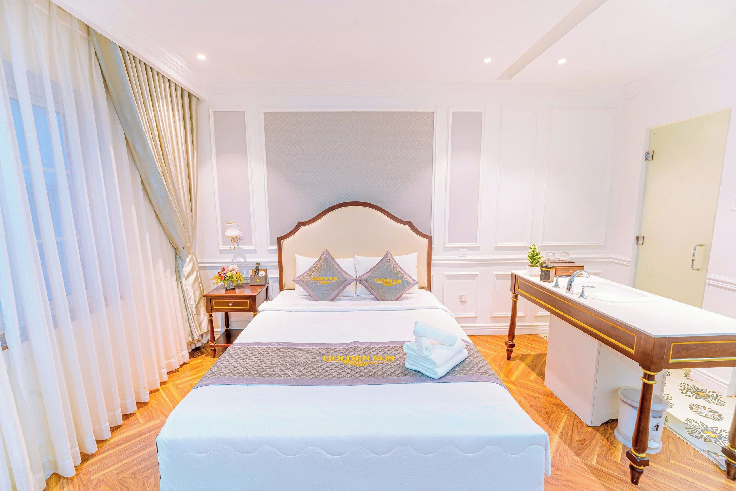 Quarto de hotel com uma cama grande, mesa de cabeceira, escrivaninha e janela com cortinas.