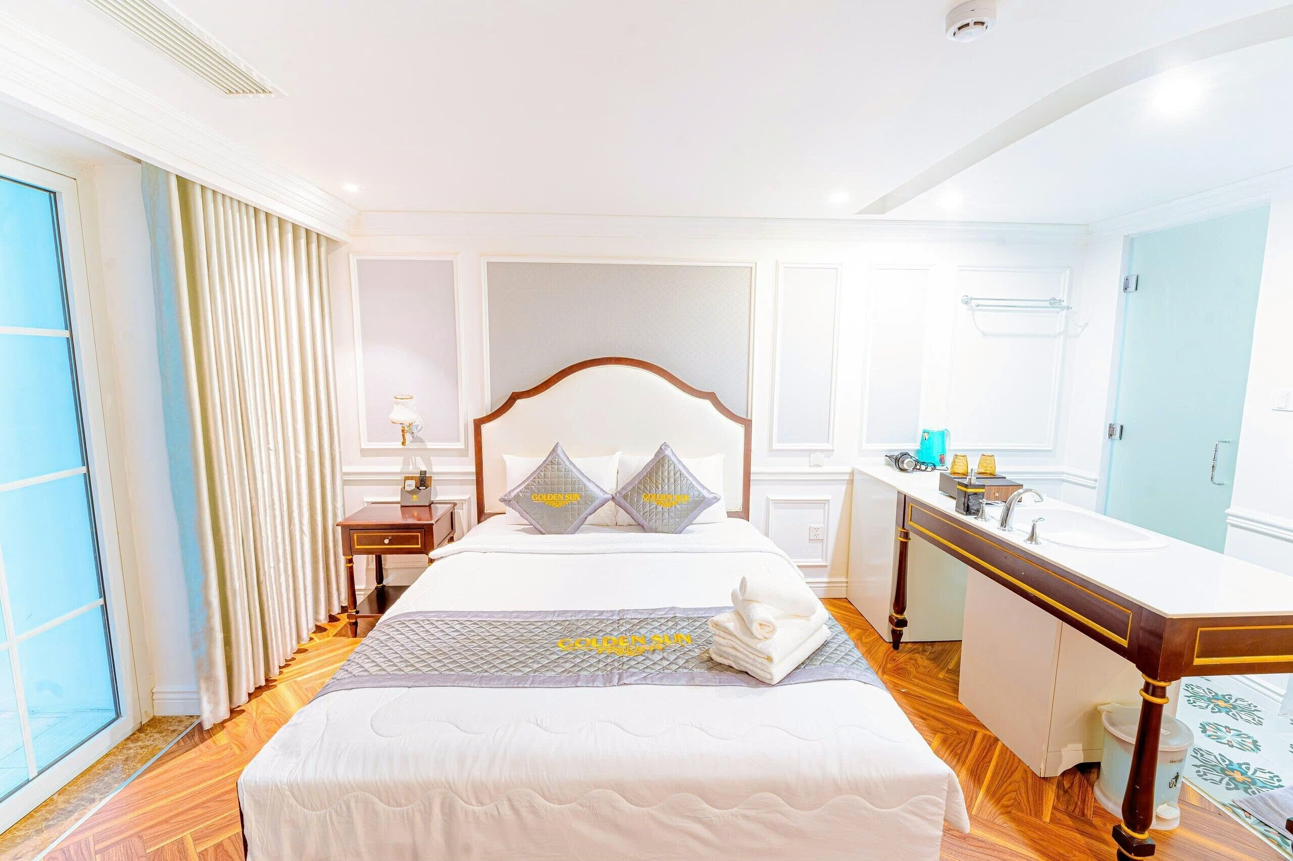 A hotel room with a large bed, a bedside table with a lamp, a bathroom with a sink and mirror, and a view of the outside through the window.