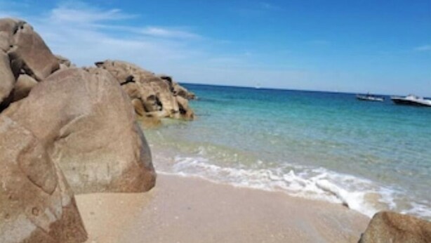 A beach with large rocks and clear blue water.