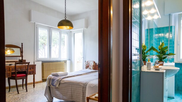 Un dormitorio con una cama, un escritorio, una silla, un radiador y una ventana.