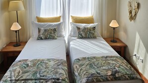 A room with two beds, white bedding, a macrame wall hanging, and a wooden ceiling.