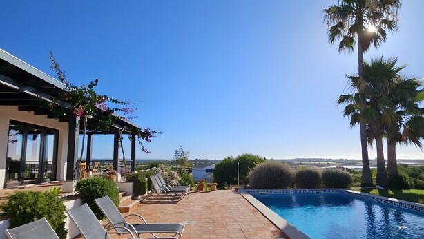A poolside area with lounge chairs, a clear blue sky, and a view of the landscape.
