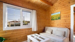 Ett rum med träpanel på väggarna, en vit soffa, ett bord med glasskiva och en målning av solrosor.