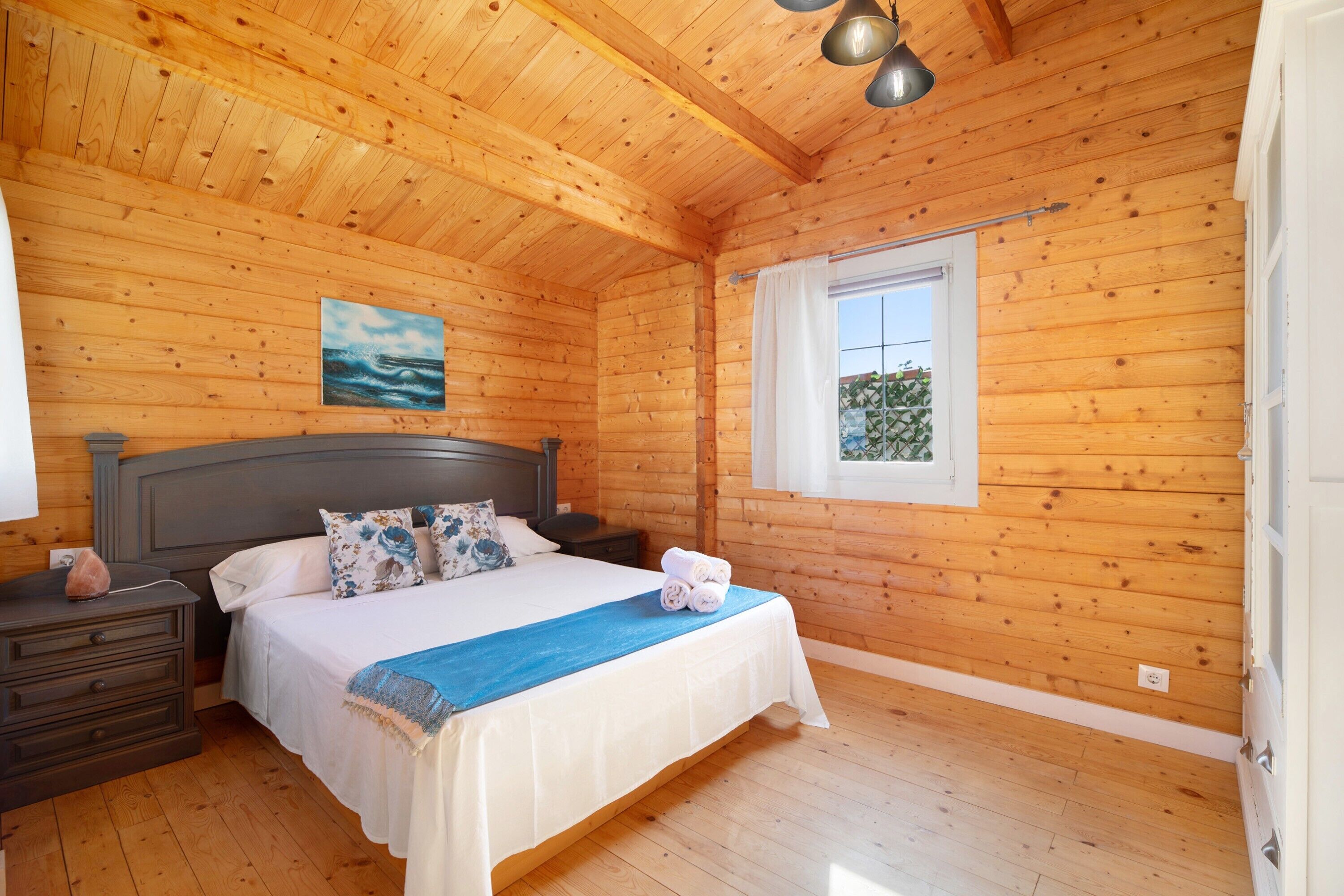 Une chambre dans une cabane en bois, avec un lit, des tables de chevet, une fenêtre et un tableau.