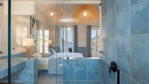 A modern bathroom with blue tiles, a glass shower enclosure, and a visible showerhead. - THIMARI. Unique location, one min from the beach! (Asos)