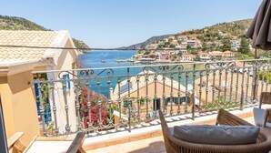 A balcony with wicker furniture, a view of the sea, and buildings in the background. - THIMARI. Unique location, one min from the beach! (Asos)