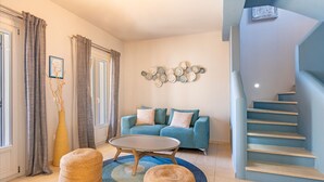 A living room with a blue sofa, a round coffee table, and a staircase. - THIMARI. Unique location, one min from the beach! (Asos)