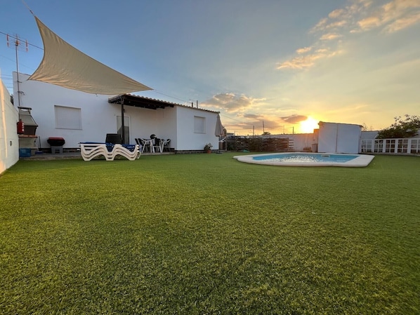 Ein Garten mit Kunstgrasanlage, einem Pool, Gartenmöbeln und einem weißen Gebäude mit Terrasse.