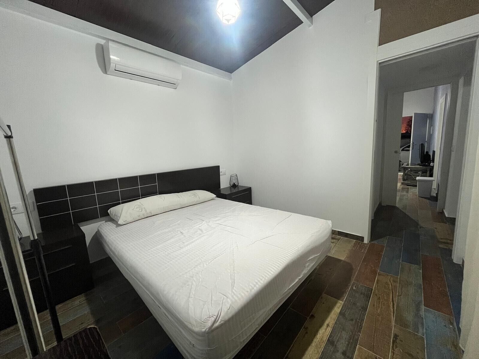 Un dormitorio con cama, mesita de noche, equipo de aire acondicionado y piso de baldosas.