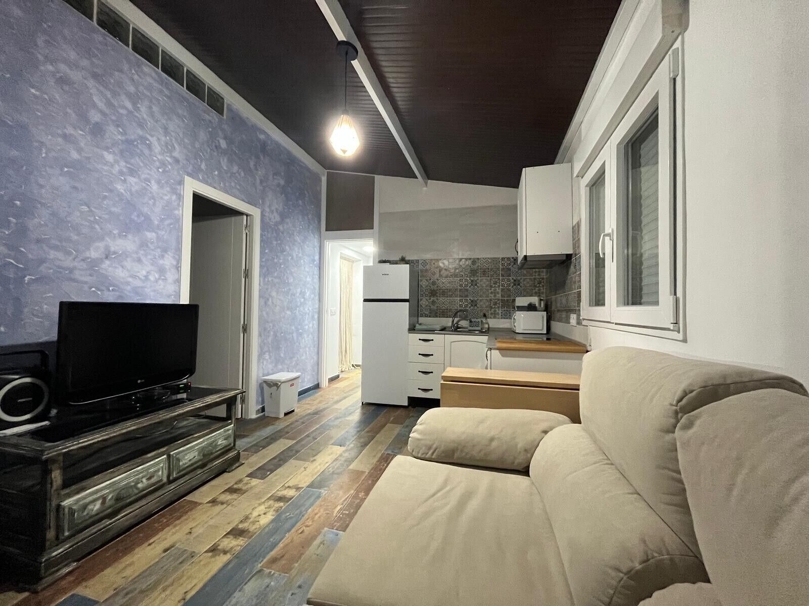 A living room with a television, sofa, and a kitchen in the background.