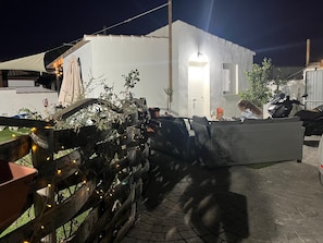 A building with a white exterior, a paved patio, and a wooden fence with string lights. - Holiday Home 'Villa Roulotte' with Shared Pool, Shared Garden and Wi-Fi (Chiclana de la frontera)
