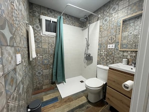 Ein Badezimmer mit gemusterten Fliesen, einer Dusche, einer Toilette und einem hölzernen Waschtisch.