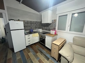 A compact kitchen with white cabinets, a built-in oven, a sink, and a window with blinds. - Holiday Home 'Villa Roulotte' with Shared Pool, Shared Garden and Wi-Fi (Chiclana de la frontera)