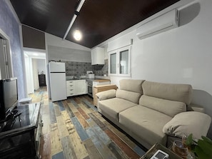 A compact living space with a kitchenette, a sofa, a TV, and a wooden floor. - Holiday Home 'Villa Roulotte' with Shared Pool, Shared Garden and Wi-Fi (Chiclana de la frontera)