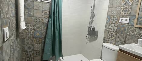 A bathroom with patterned tiles, a shower, a toilet, a sink, and a mirror.
