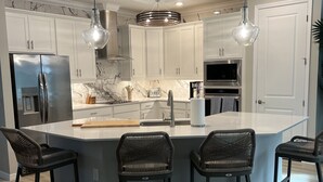Une cuisine moderne avec des meubles blancs, un îlot central doté de tabourets, des appareils en acier inoxydable et un éclairage suspendu.