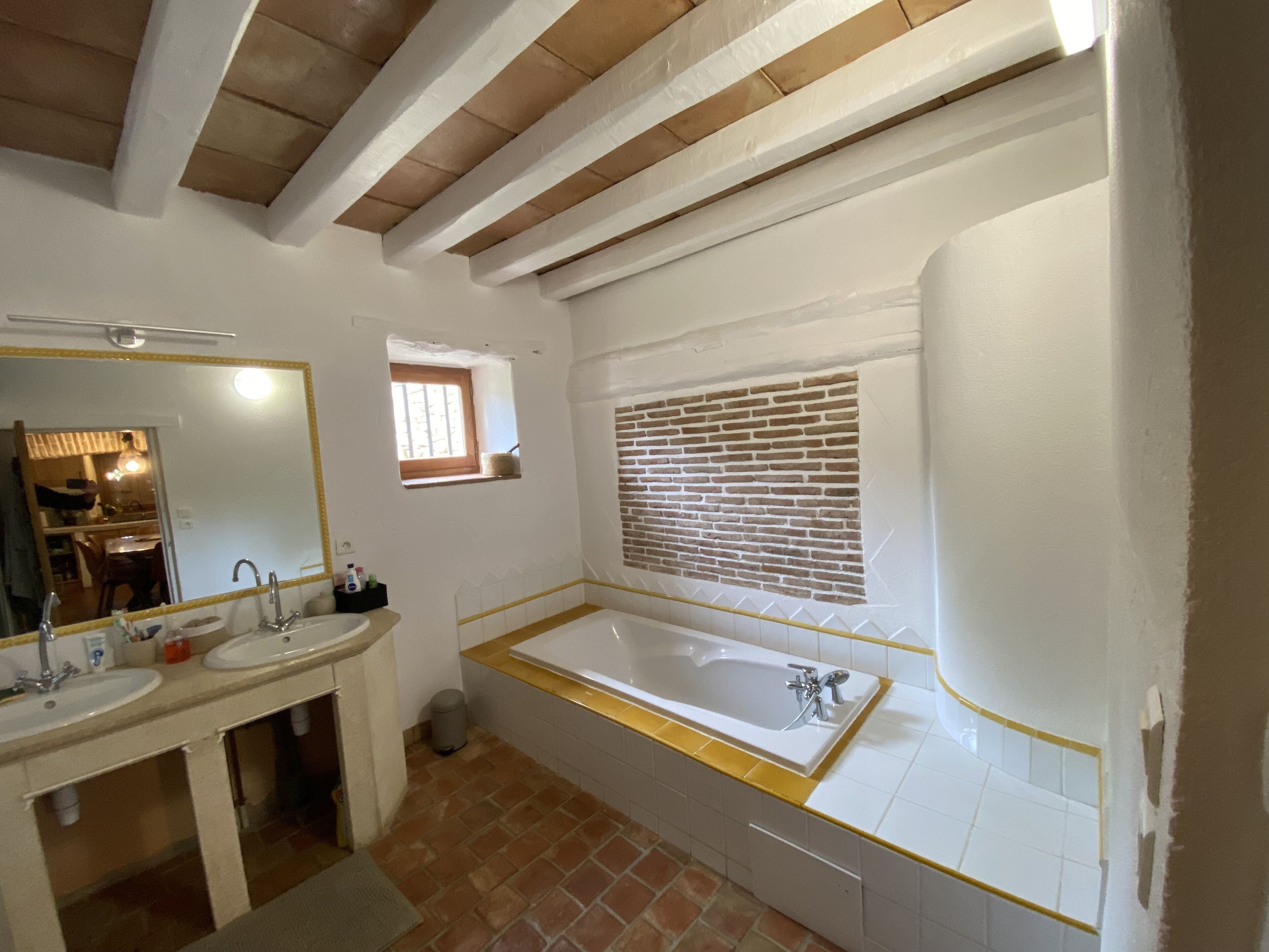 A bathroom with two sinks, a bathtub, a window with a brick pattern, and a small window above the sink.