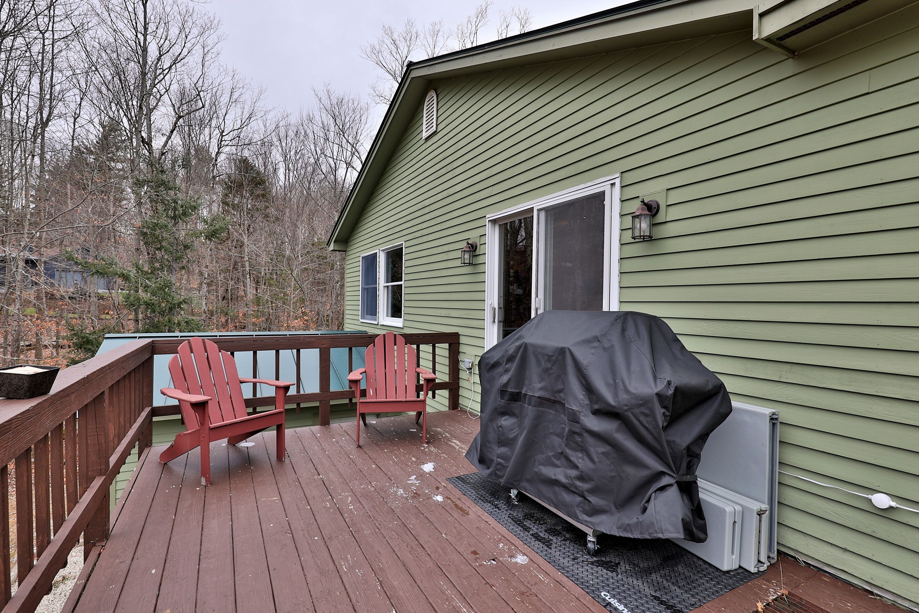 A green house with a deck, two red Adirondack chairs, and a covered grill.
