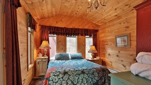 A wooden cabin bedroom with a bed, two bedside lamps, a chandelier, and a window with curtains. - The Tanglewood Lodge: Amazing Ski Home For Groups. Hot Tub. Close To Killington Resort! 4 Bedroom Home (Killington)