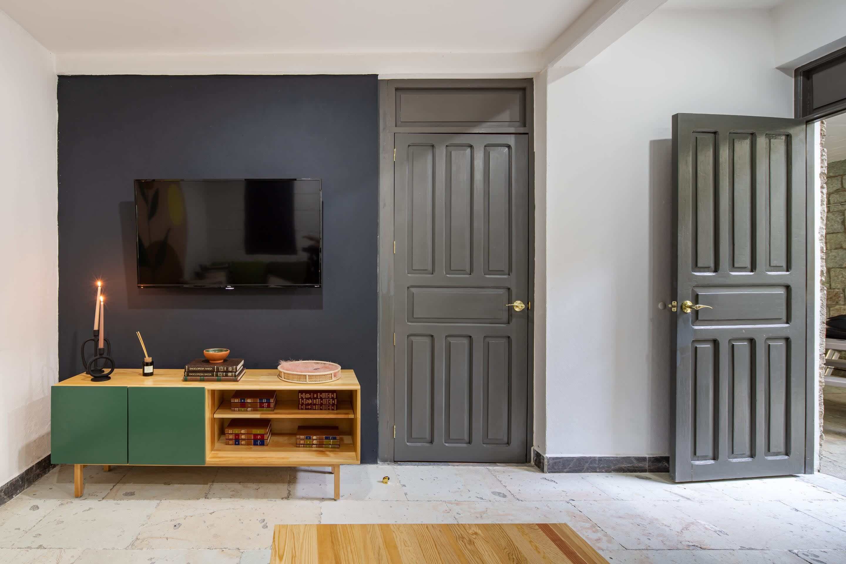 Une pièce avec un mur sombre, une bibliothèque en bois remplie de livres, un téléviseur à écran plat et une porte grise fermée.