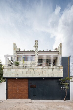 A modern building with a wooden garage door, a balcony with a metal railing, and a black wall with a security camera. - Rooftop Hot Tub! 3 levels, 5Bedroom in Villa Noria (Oaxaca de Juárez)