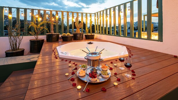 Une terrasse sur le toit dotée d’un jacuzzi, entourée de plantes en pot et illuminée de guirlandes lumineuses.