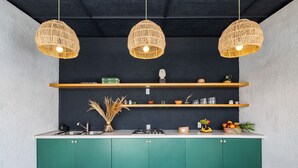 Une cuisine avec des meubles de couleur verte, trois suspensions en osier et des étagères en bois au-dessus.