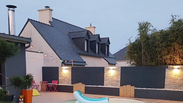 Una propiedad residencial con piscina, mobiliario exterior y una casa grande con techo inclinado.