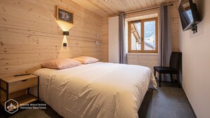 Ein Schlafzimmer mit Holzwänden, einem Bett, einem Nachttisch, einer Lampe, einem Fernseher und einem Fenster mit Vorhängen.