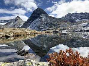 Un lago de montaña con reflejos nítidos, rodeado de terreno rocoso y picos nevados.