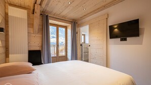 Ein Schlafzimmer mit einem Bett, einem an der Wand montierten Fernseher und einem Fenster mit Vorhängen.