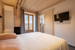 A bedroom with a bed, a TV mounted on the wall, and a window with curtains. - Le Temps Suspendu - "Anémone" Charming apartment - 8 people (Termignon, Val-Cenis)