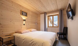 Een slaapkamer met houten lambrisering, een bed, nachtkastje, lamp, televisie en raam met gordijnen.