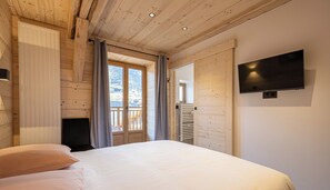 Een slaapkamer met een bed, een aan de muur bevestigde televisie en een raam met gordijnen.