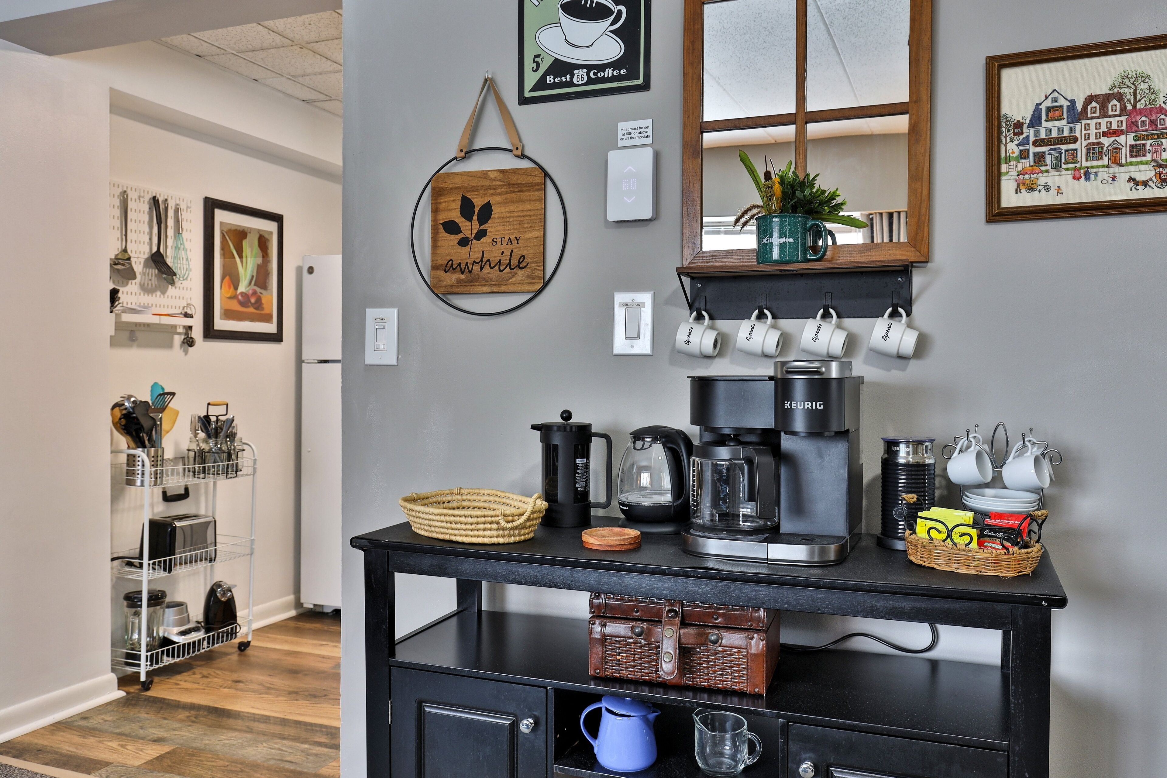 A kitchen area with a coffee station, a hanging sign that says "STAY awhile", and a wall-mounted coffee machine.
