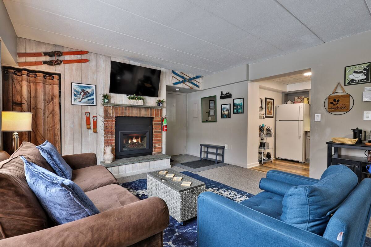 Ein Wohnzimmer mit Kamin, Sofas, einem Couchtisch und einem an der Wand befestigten Fernseher.