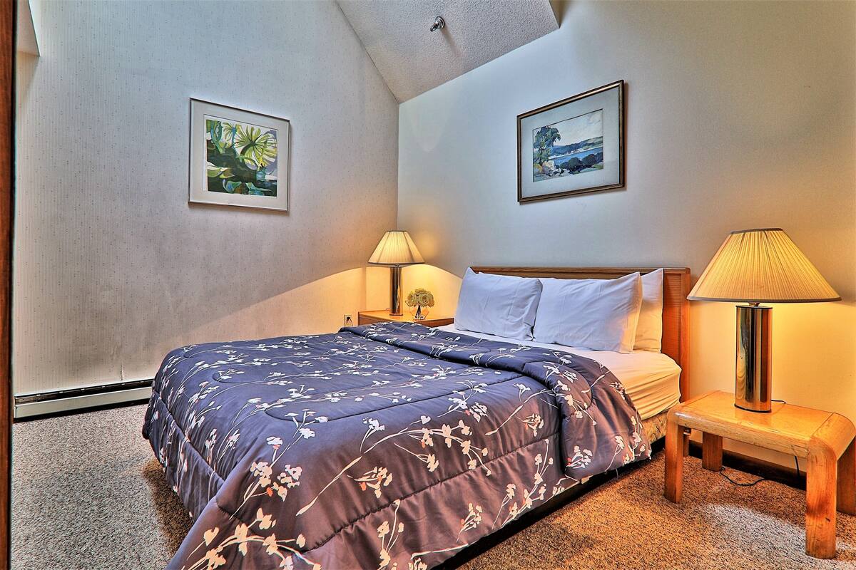 Ein Schlafzimmer mit einem Bett, zwei Nachttischen, einer Deckenleuchte und zwei gerahmten Bildern an den Wänden.