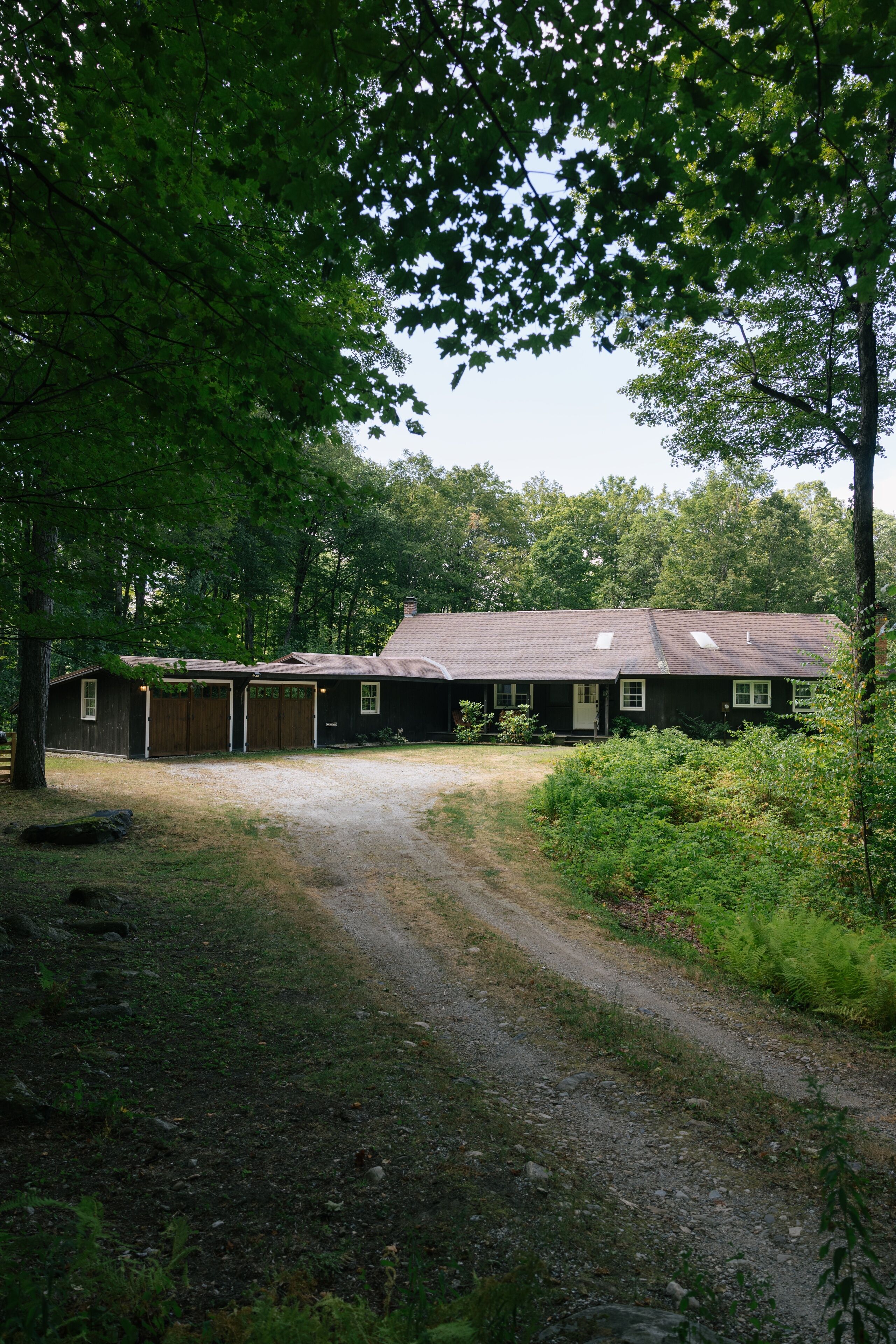 A two-story house with a garage, surrounded by trees and a gravel driveway.