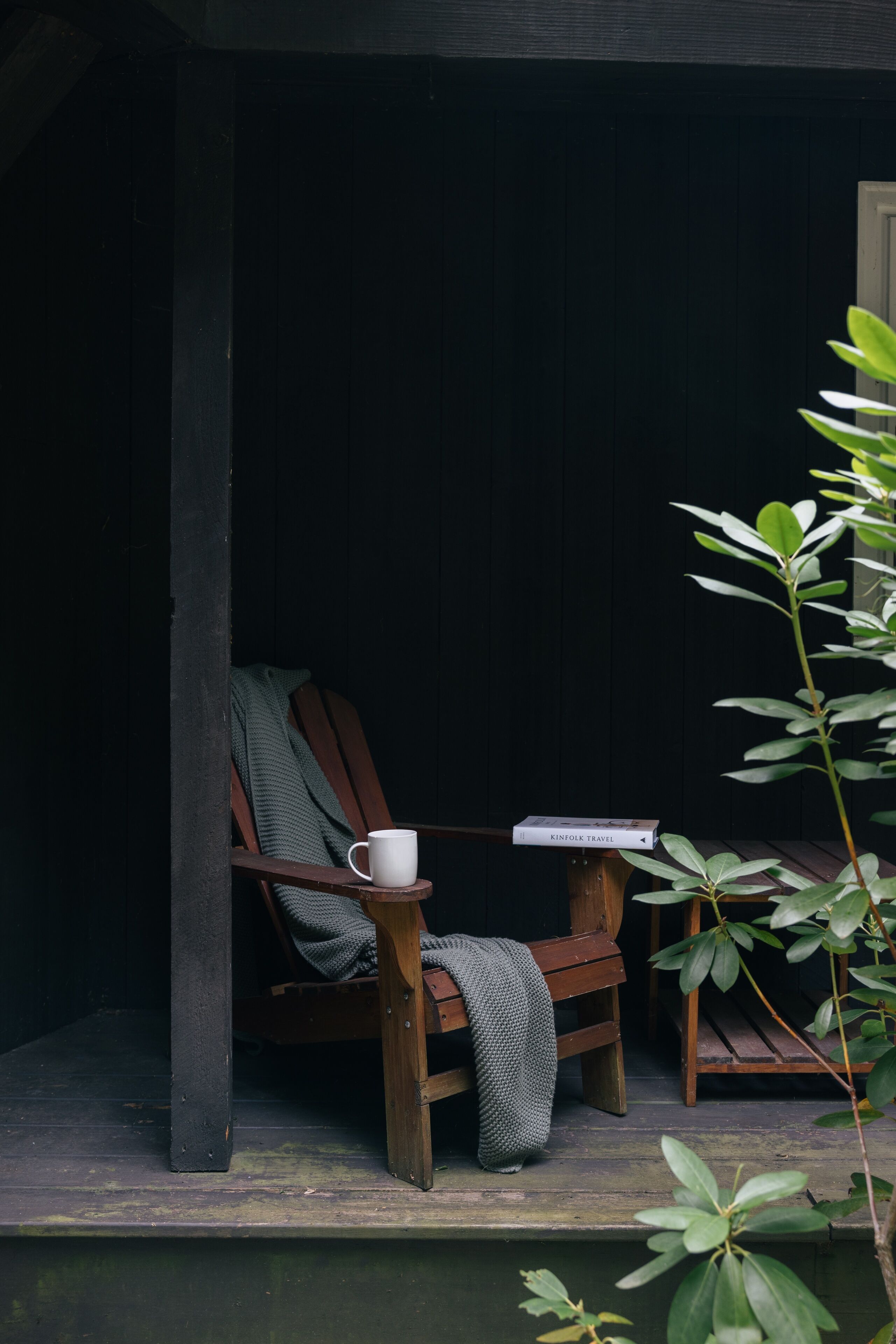 Une chaise en bois, une tasse blanche et un livre intitulé « KINFOLK TRAVEL » sont posés sur une véranda.