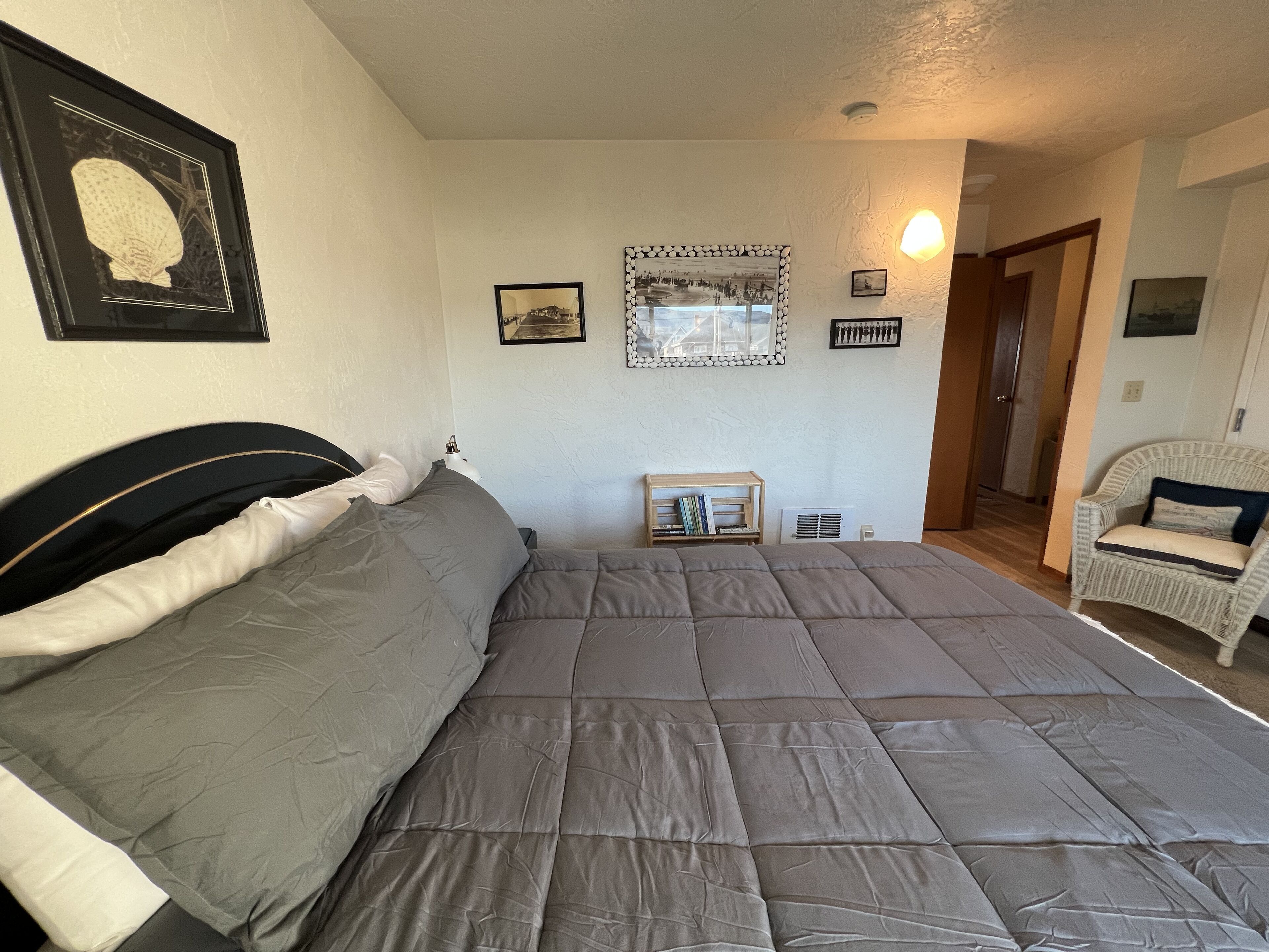A bedroom with a large bed, a chair, a mirror, and framed pictures on the wall.