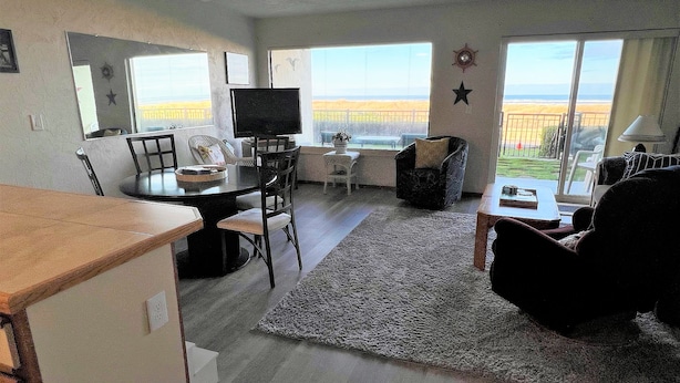 A spacious living room with a dining area, large windows offering a view of the beach, and a cozy seating area. - Ground floor Oceanfront 2 blocks from downtown shopping and eateries (Seaside)