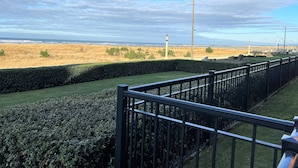 A view from a balcony overlooking a grassy field with a hedge and a metal railing. - Ground floor Oceanfront 2 blocks from downtown shopping and eateries (Seaside)